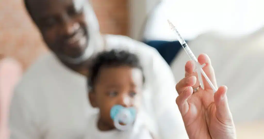 father holds toddler son preparing for childhood vaccine. Syringe in doctor's hand.