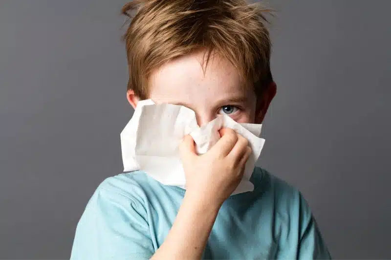 young boy blowing nose from allergies