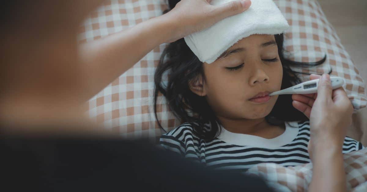 Child with fever in bed, getting temperature checked by parent