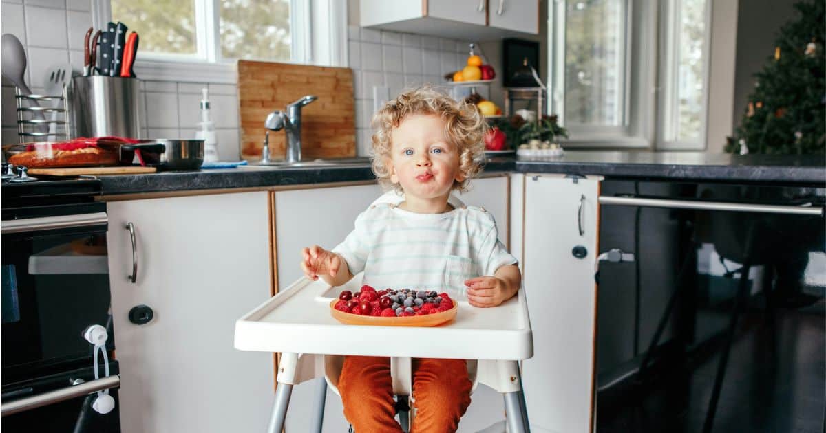 young child eating fruit in high chair